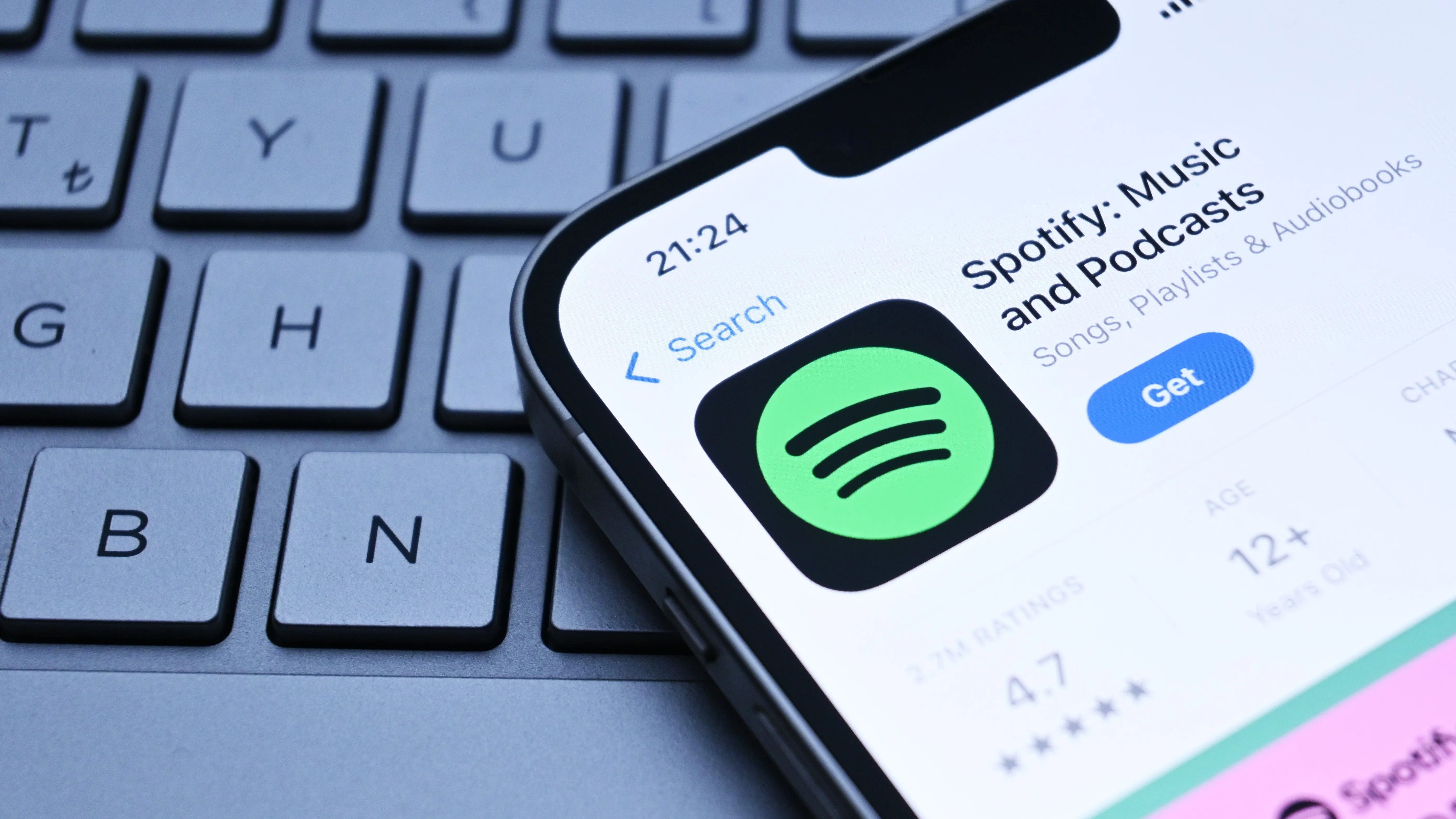 An iPhone showing Spotify in the Apple app store, laying on top of a laptop keyboard 